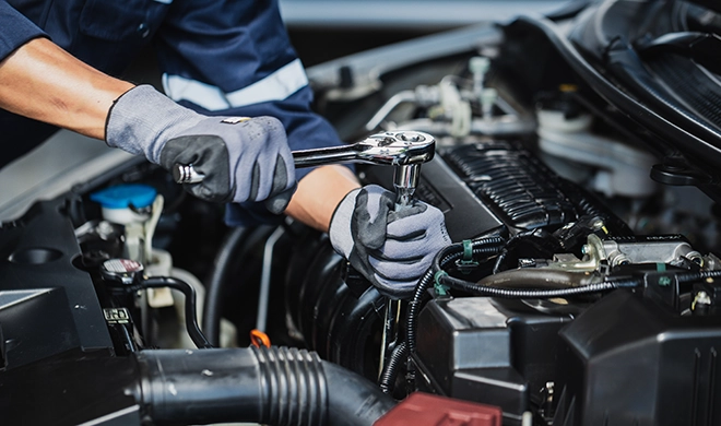 A photo of two gloved hands using a socket wrench on a car engine