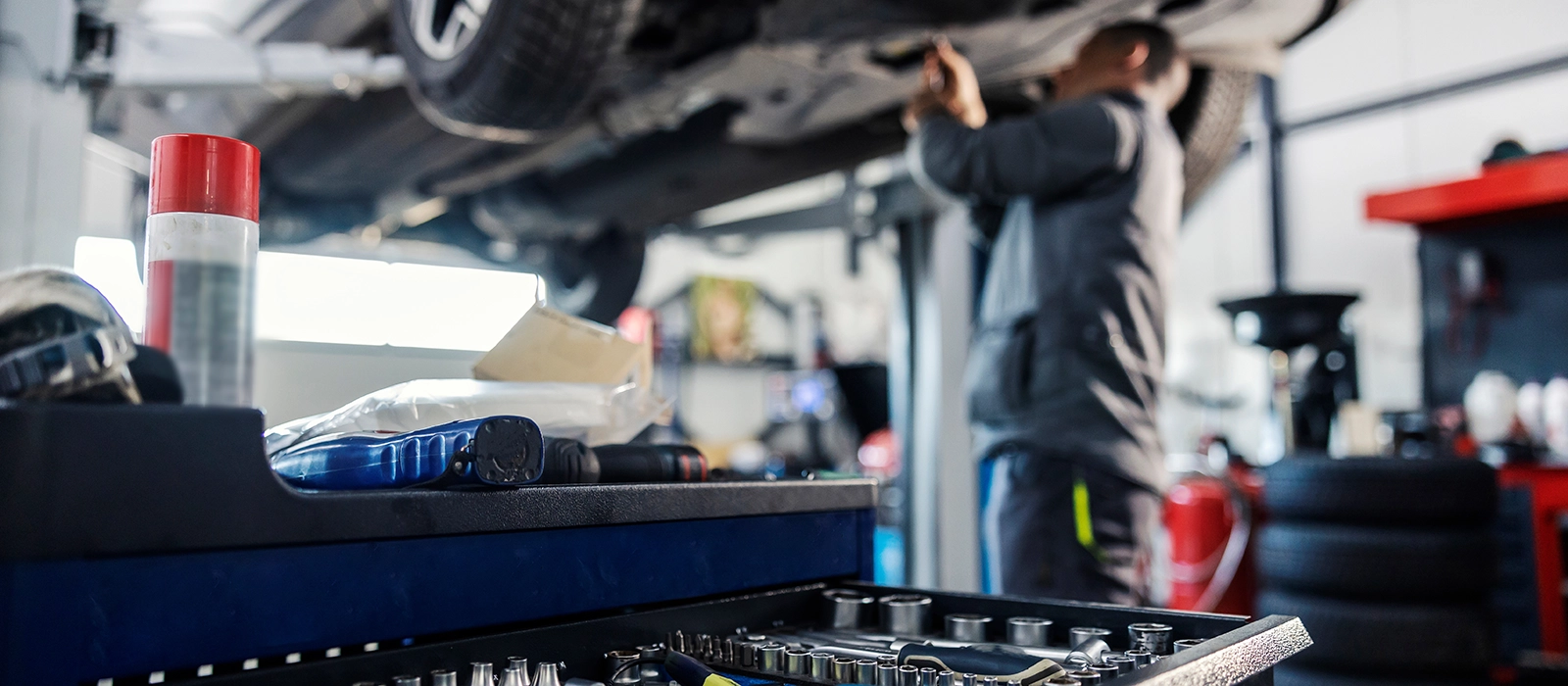 A blurred photo of a man working underneath a car on a lift